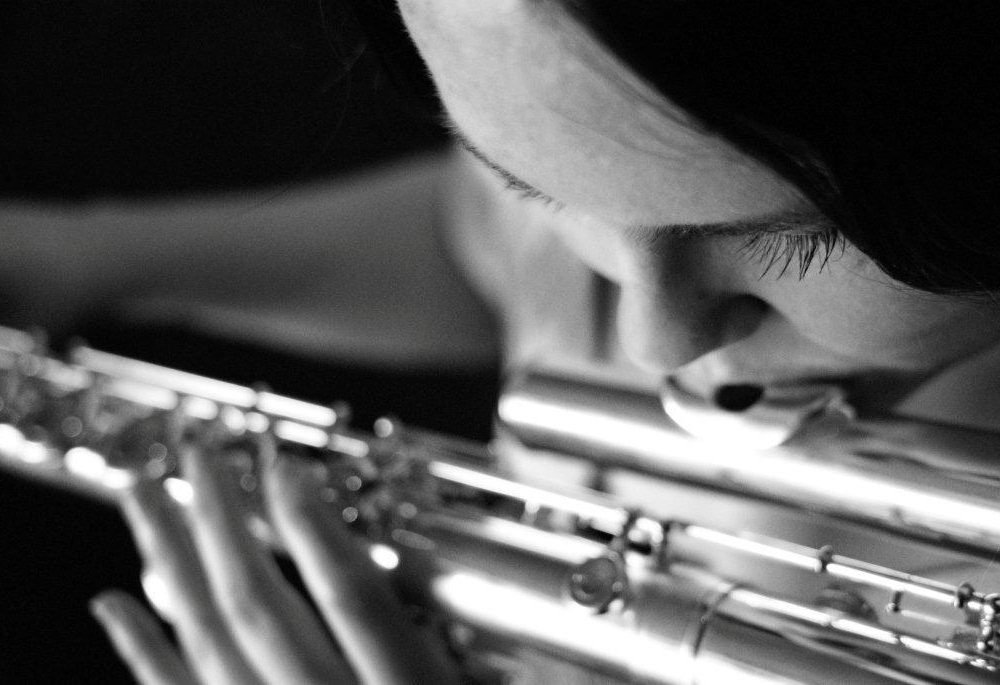 A close up of a dark haired woman, Morwenna, playing the flute. The photo is in black and white.